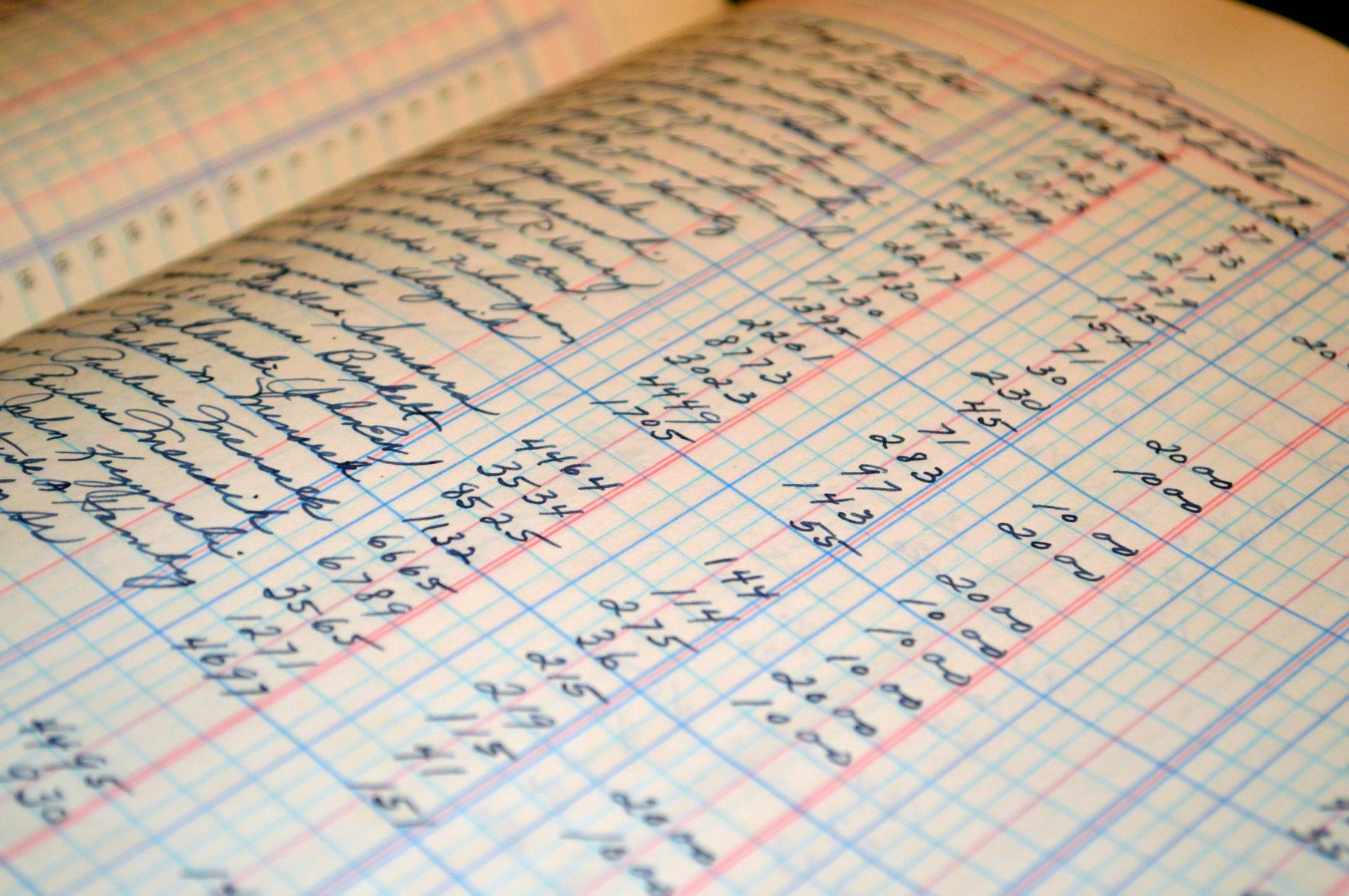 Close-up of a handwritten notebook page with blue lines and red margin, filled with notes and numbers.