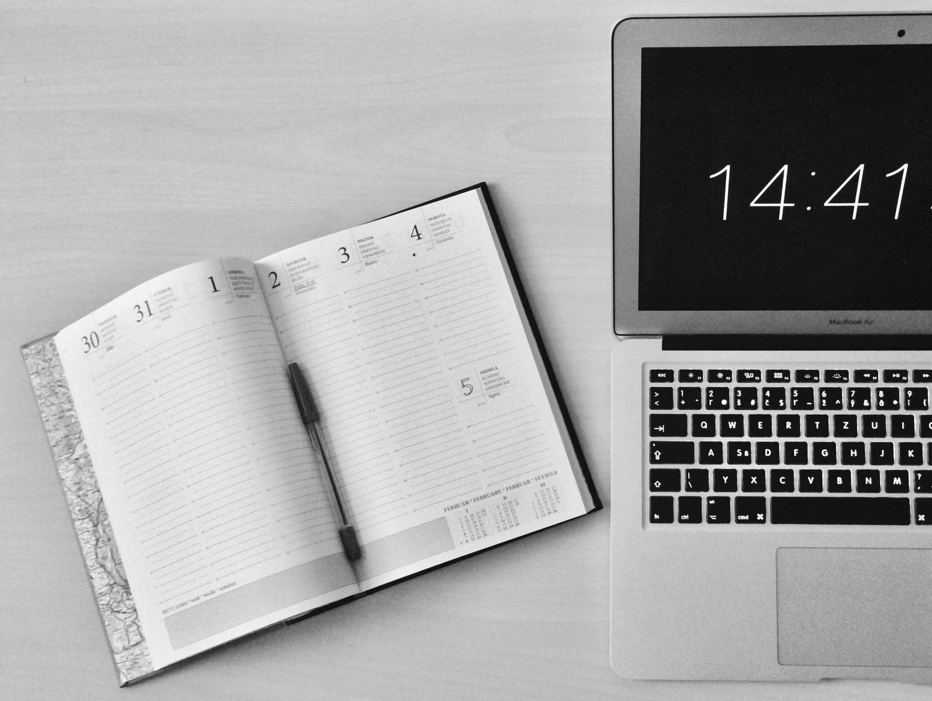Open notebook beside a laptop showing 14:41 on a desk
