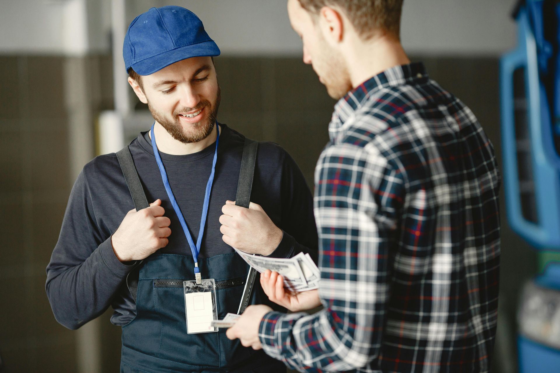 Two men in work clothes exchanging a smartphone in a workshop or office setting