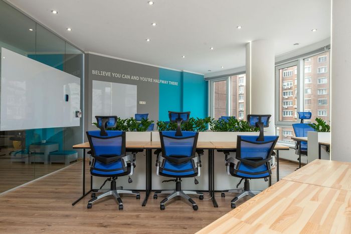 Modern office meeting room with blue chairs, white tables, and glass walls overlooking city buildings