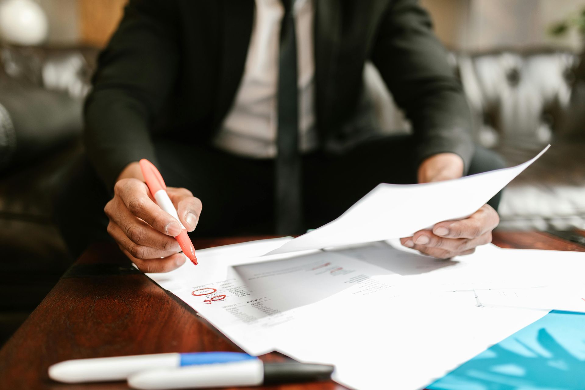 Person in a suit reviews documents at a desk with papers, pen, and blue folder.