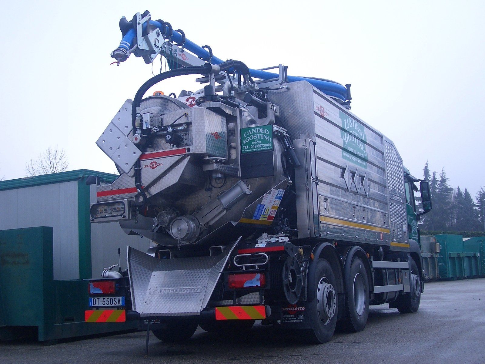 Vista posteriore di un grande camion aspiratutto color argento. Un tubo flessibile blu si estende dall'alto. L'ambientazione è all'aperto.