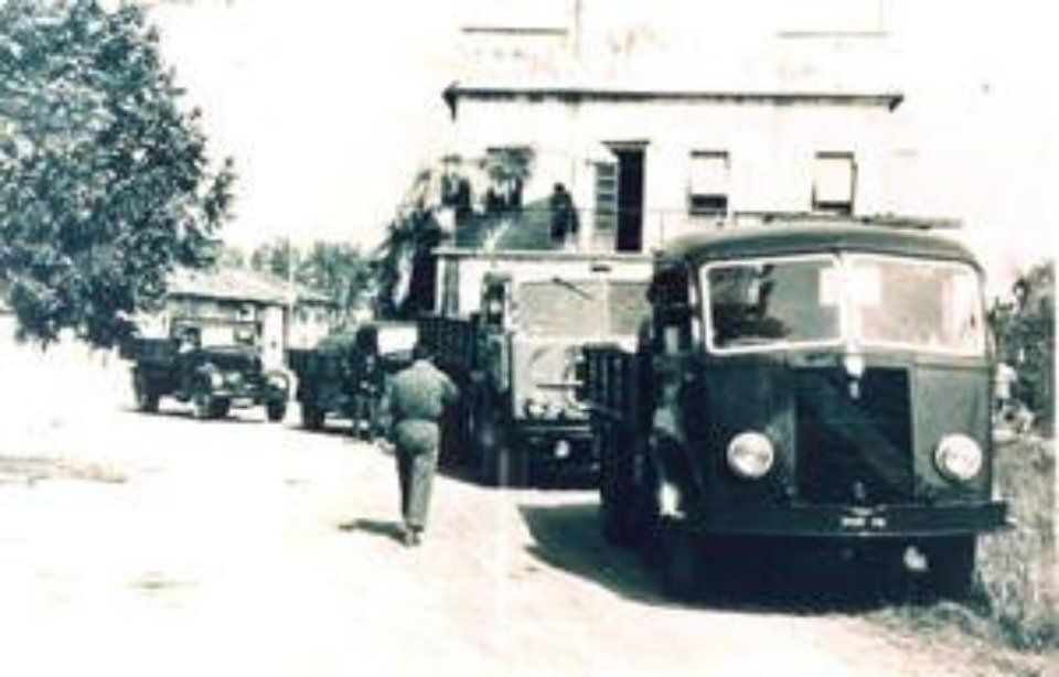 Veicoli e una persona su una strada vicino a un edificio; probabilmente un mezzo di trasporto militare.
