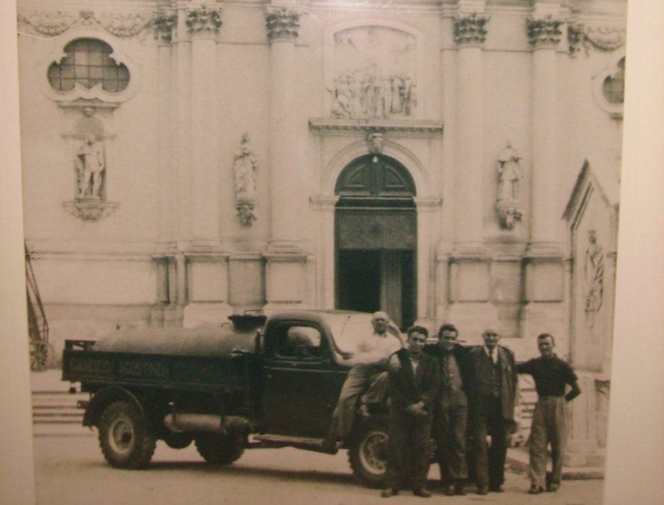 Uomini in posa con un camion davanti a una chiesa. Foto in bianco e nero d'epoca.
