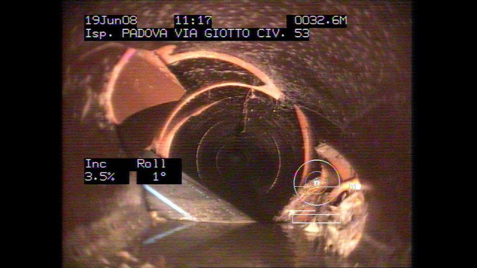 Vista della telecamera di ispezione all'interno di un tubo, che mostra danni e detriti, con sovrapposizione di testo.