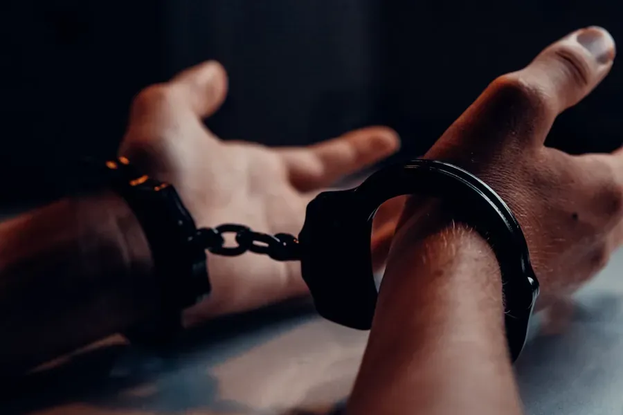 Hands in handcuffs, close-up, against a dark background.