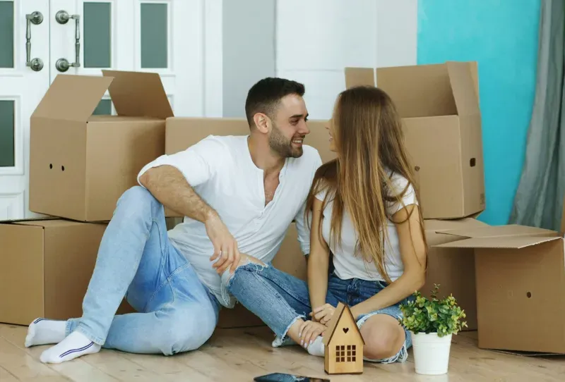 a man and woman sit on the floor of their new home, surrounded by boxes