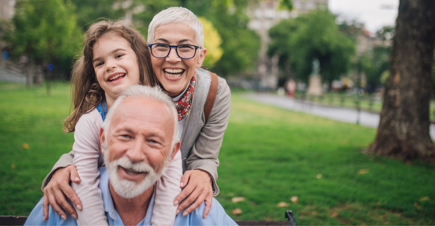 An elderly couple and a little girl are posing for a picture in a park.