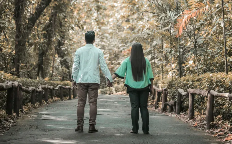 man and woman holding hands on a tree-lined walkway