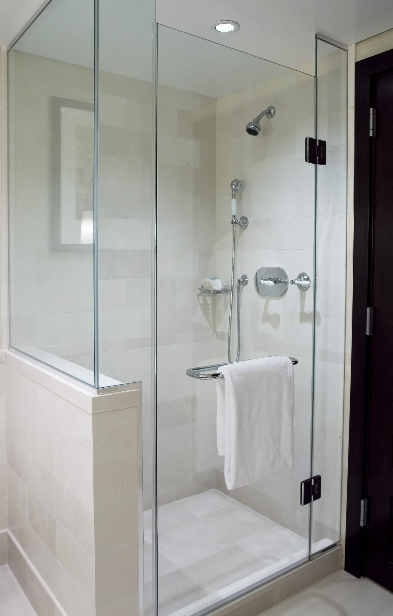 Glass shower stall with white towel hanging on the door.