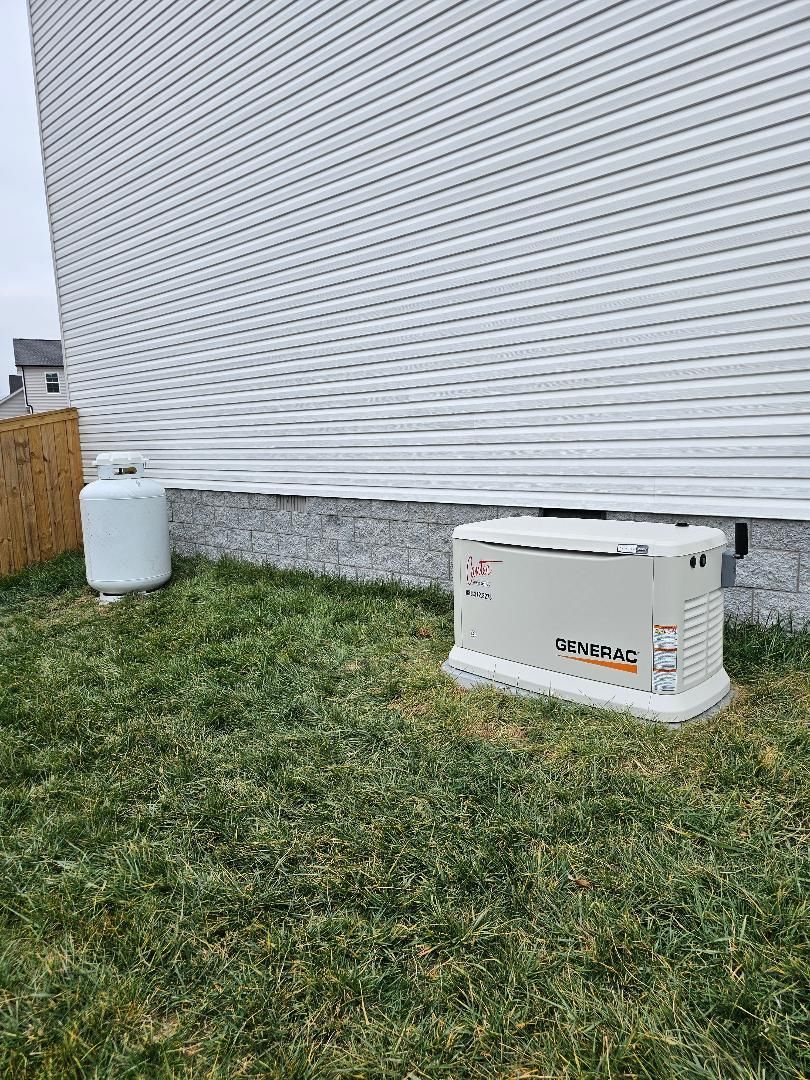 A generator and propane tank beside a building with white siding on grass.