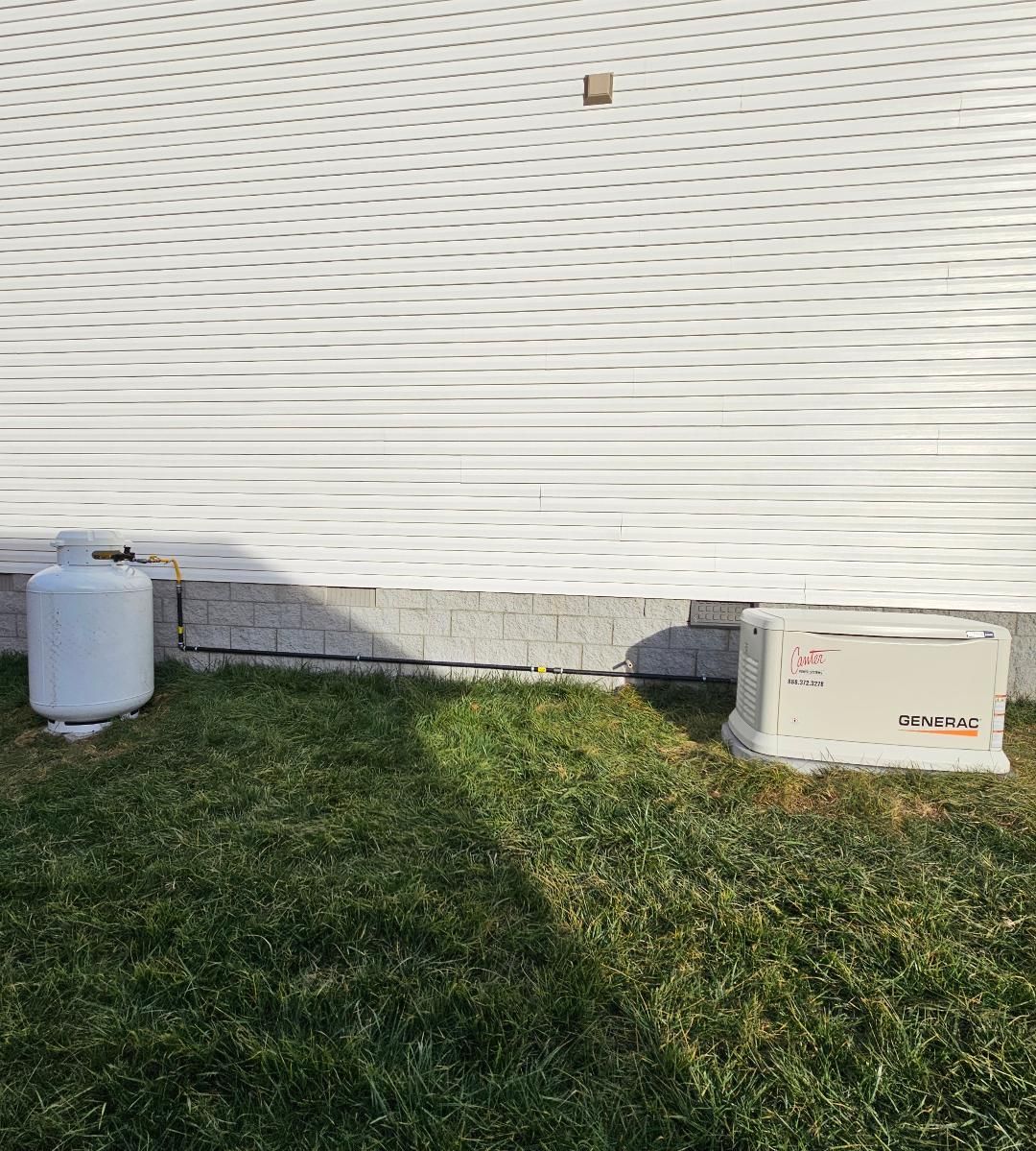 Black gas pipes run along a brick wall and connect to a beige generator unit.