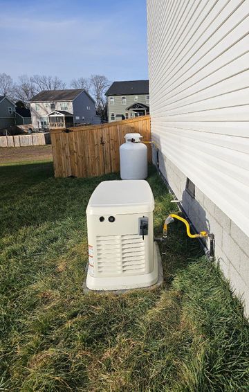 A standby generator and propane tank next to a house with wooden fence.