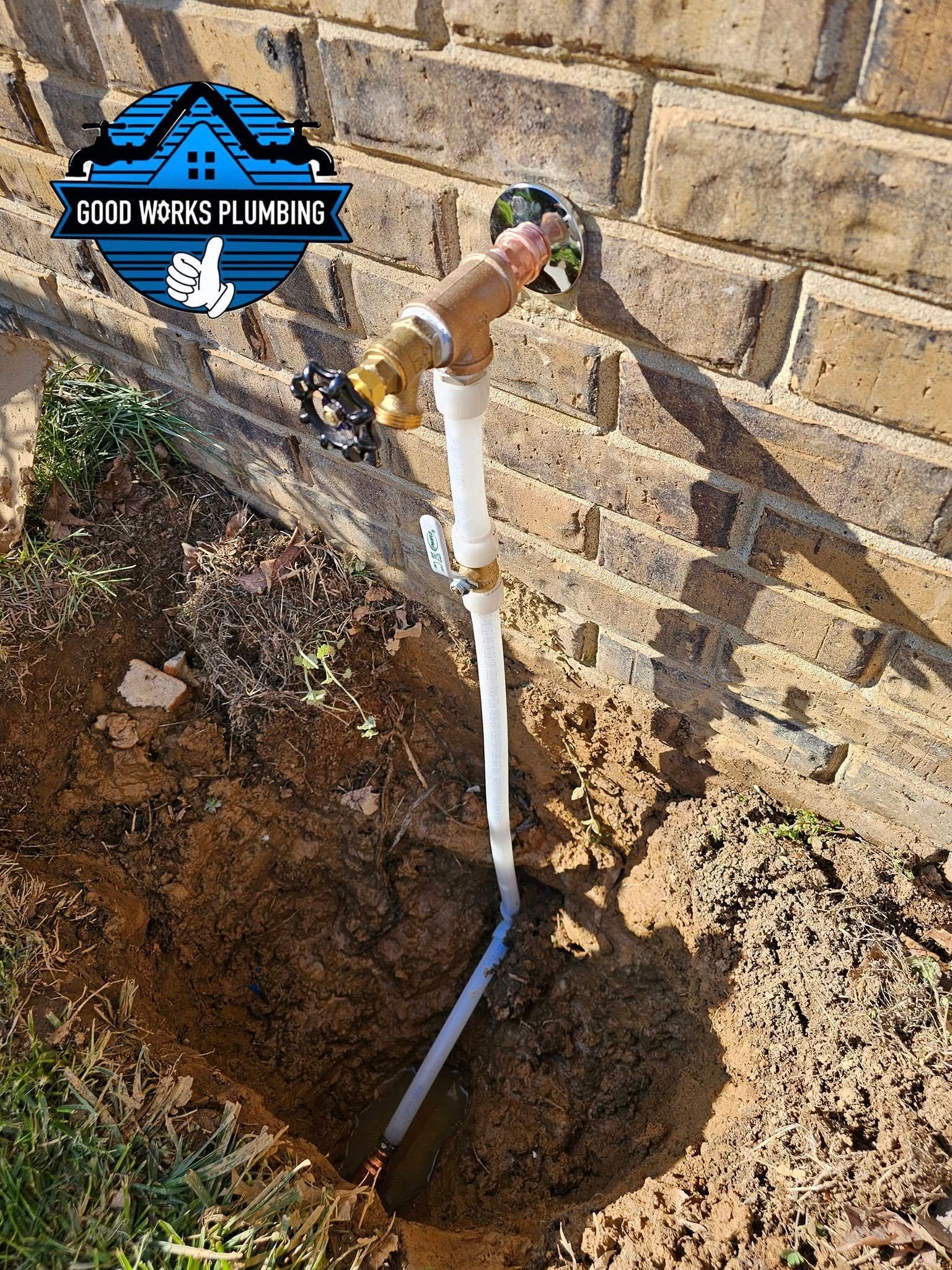 A faucet connected to a white pipe buried in a hole next to a brick wall.