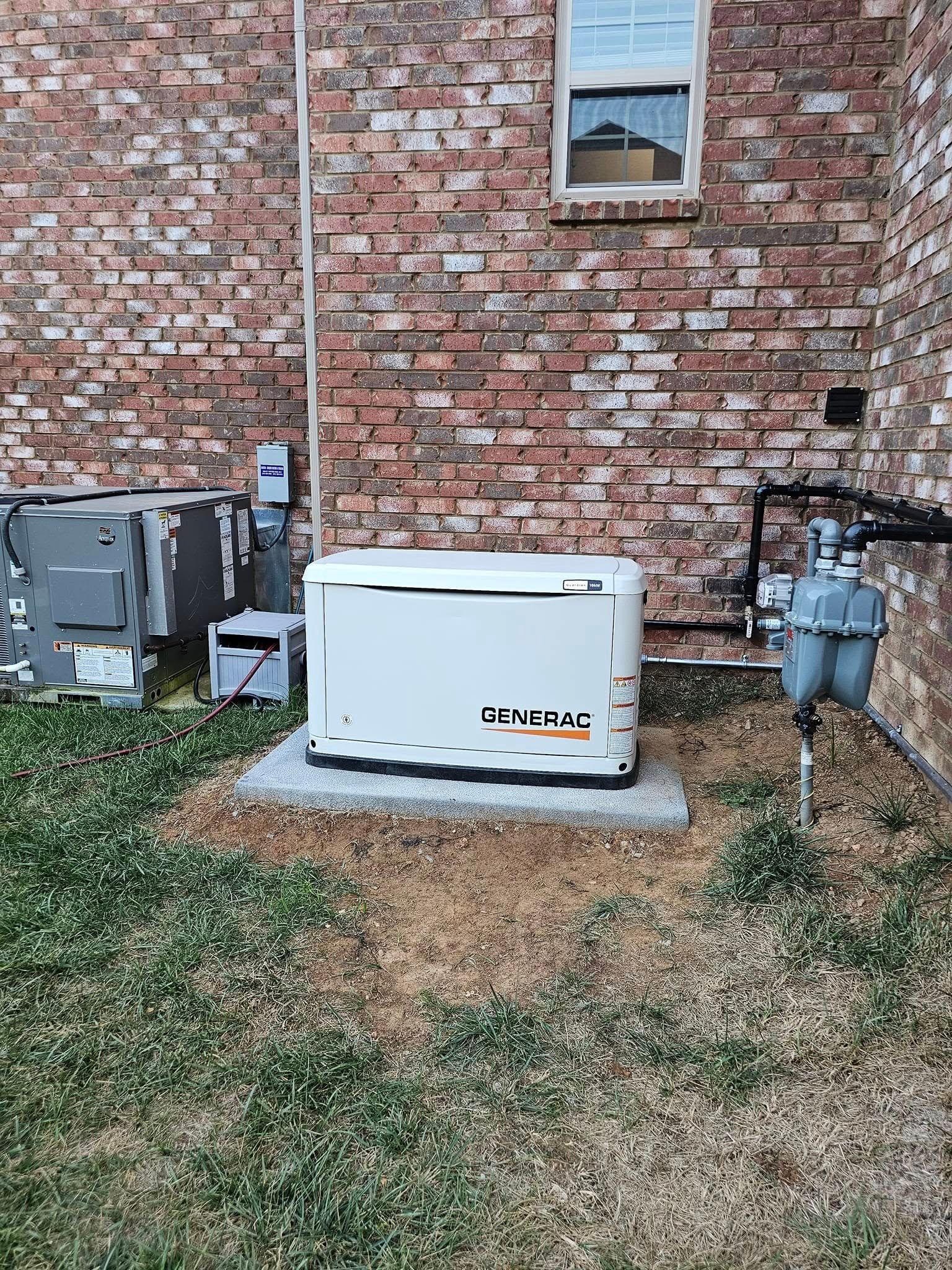 A white generator is mounted on a concrete pad next to a brick wall and a utility meter.