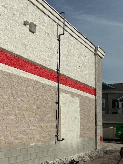 Black pipe runs vertically down a textured beige building with a red stripe. The sky is partly cloudy.