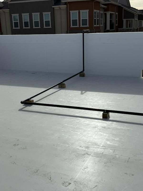 Black pipes on a white flat roof, supported by blocks. Houses are in the background.