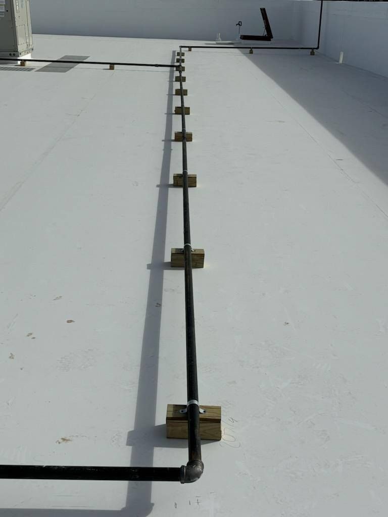 Black pipe running across a white rooftop, secured by wooden blocks.
