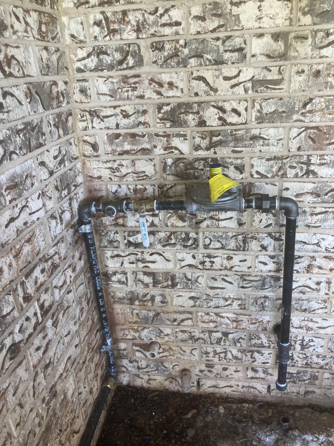 Black gas pipes attached to brick wall, with yellow shutoff valve and a manual valve.