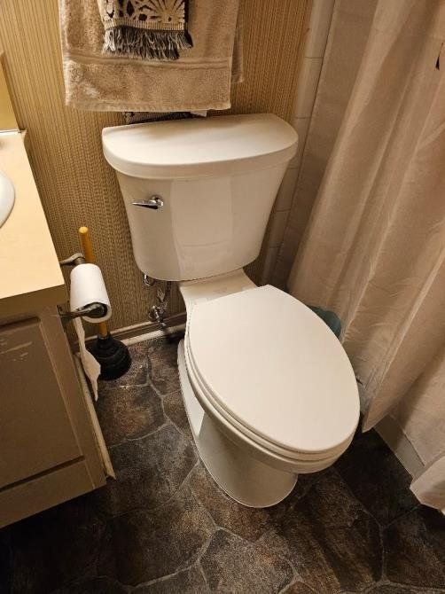 White toilet in a small bathroom with patterned wallpaper and dark flooring.