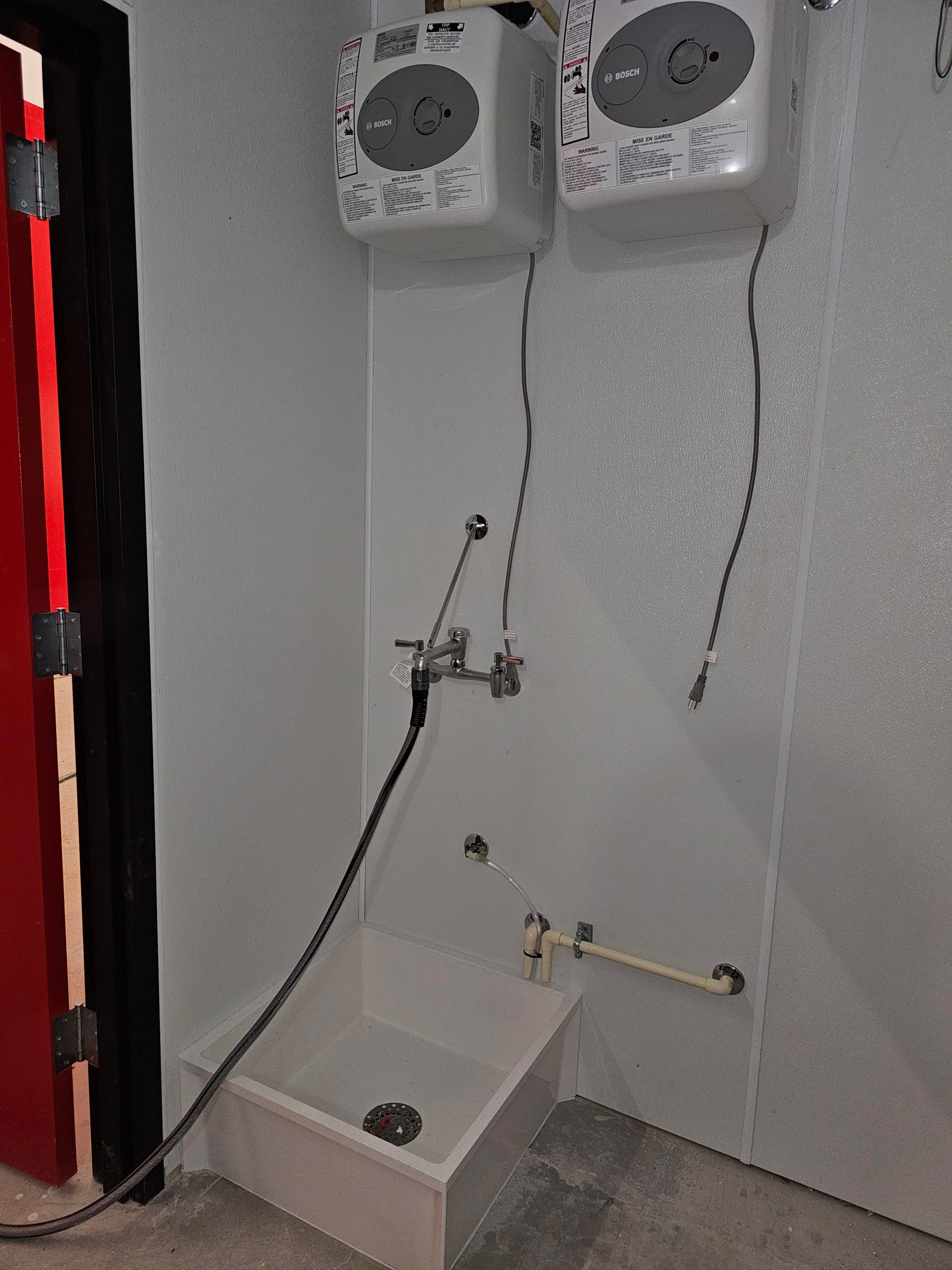Wash station with two wall-mounted soap dispensers, faucet, and a low sink. Black hose and red door frame visible.