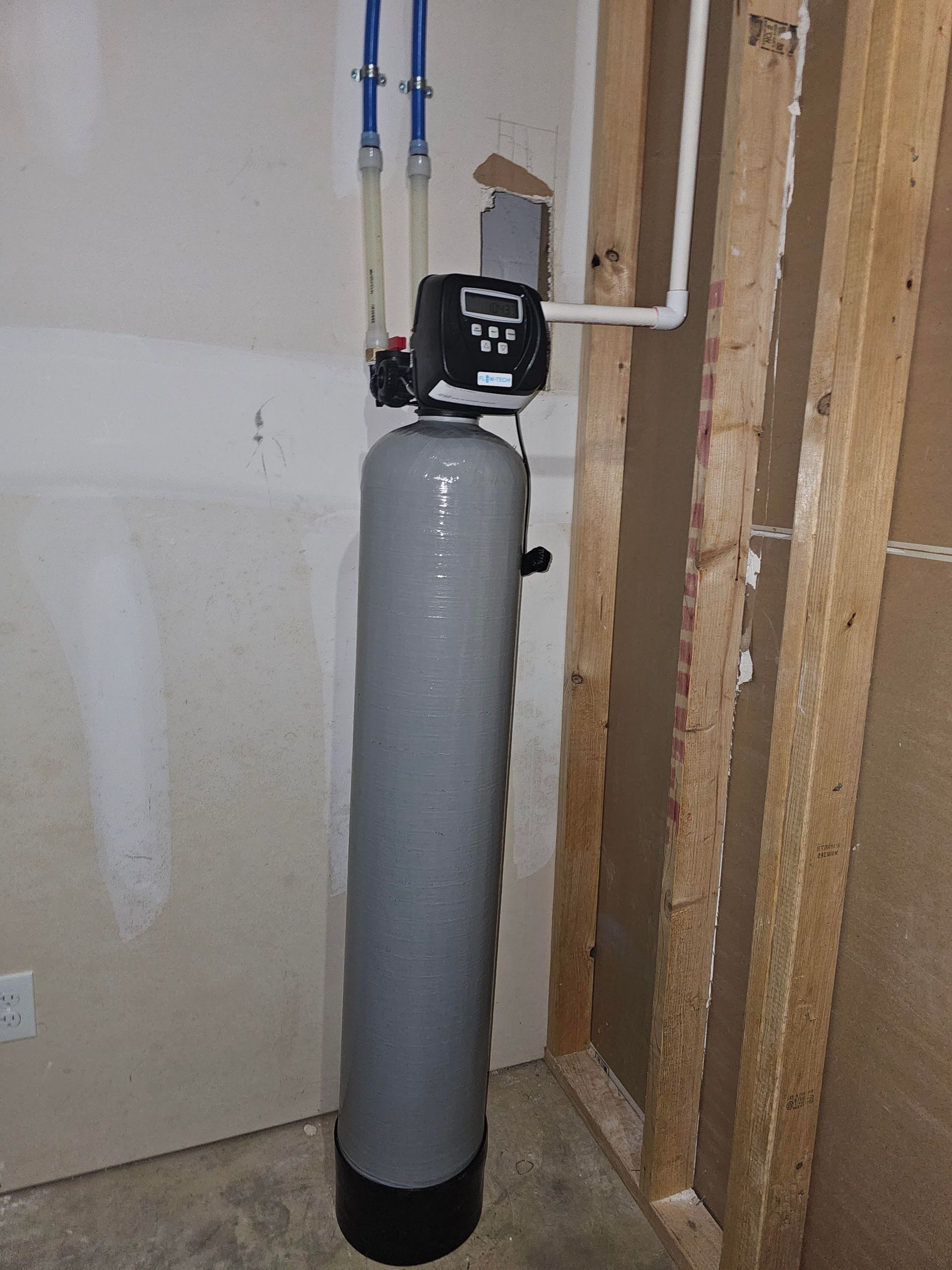 Water filter system installed inside a cabinet, featuring three white cylindrical filters with colored tubing.
