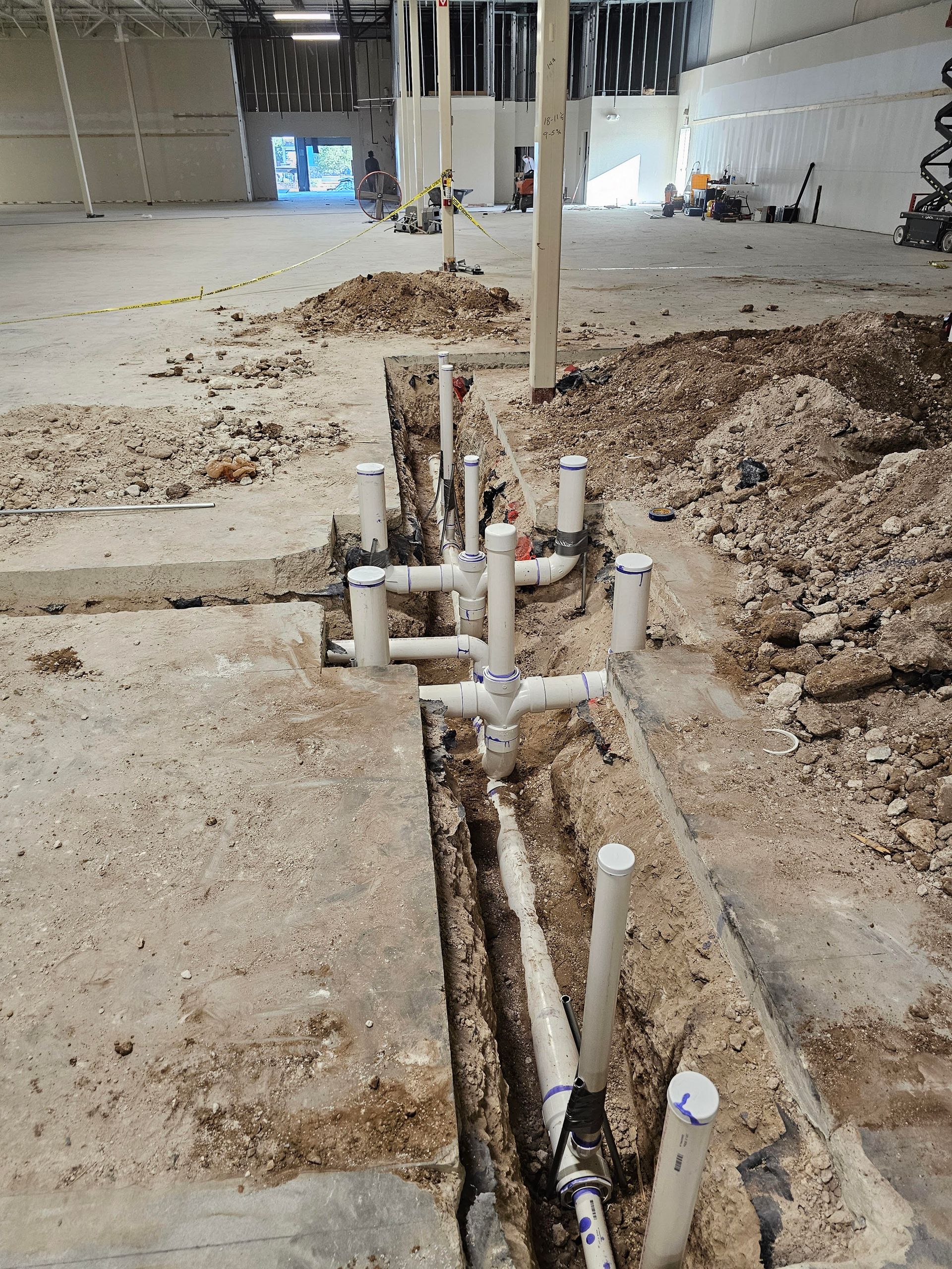 Plumbing pipes laid in a trench on a construction site. White PVC pipes with dirt and debris surround them.