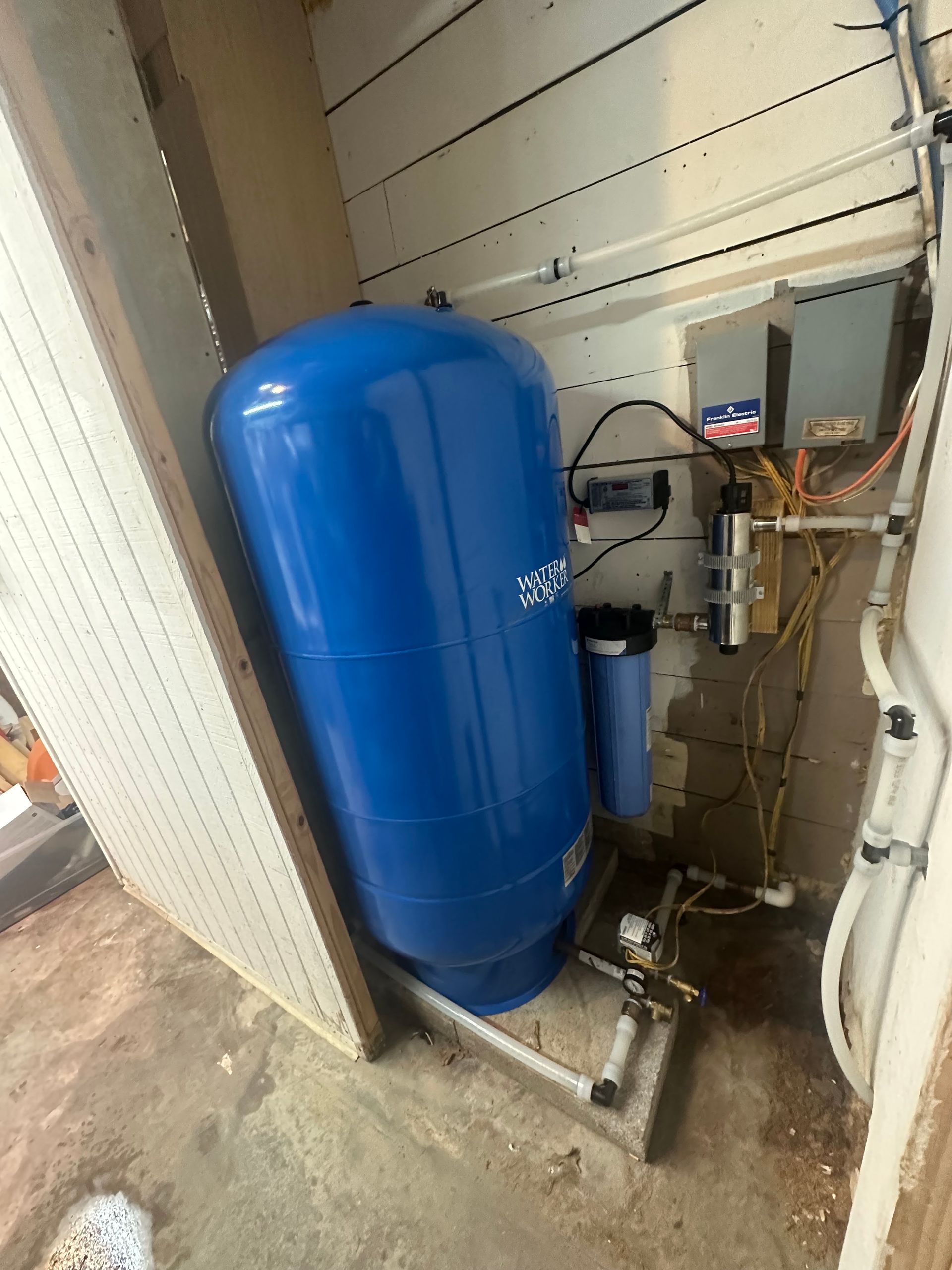 Blue water pressure tank with attached filter and control panel, in a utility room.