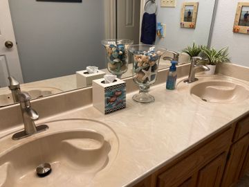 Bathroom with double sinks, seashell decor, and mirror. Beige countertops and light-colored cabinets.
