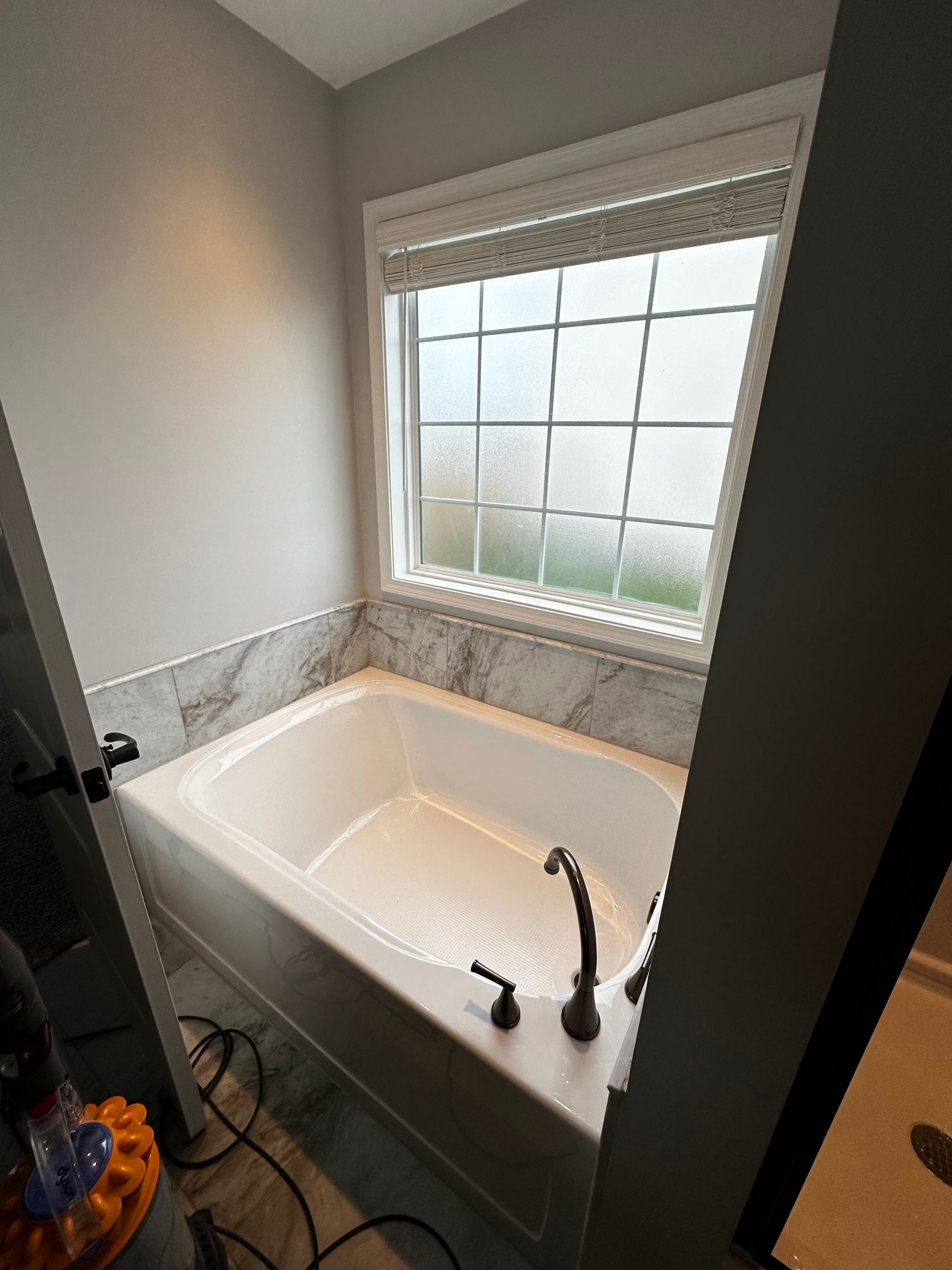 White bathtub in a bathroom with a window above it. Gray walls and marble tile are visible.