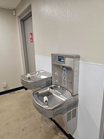 Person using a plunger in a sink filled with brown water, other tools and yellow gloves nearby.