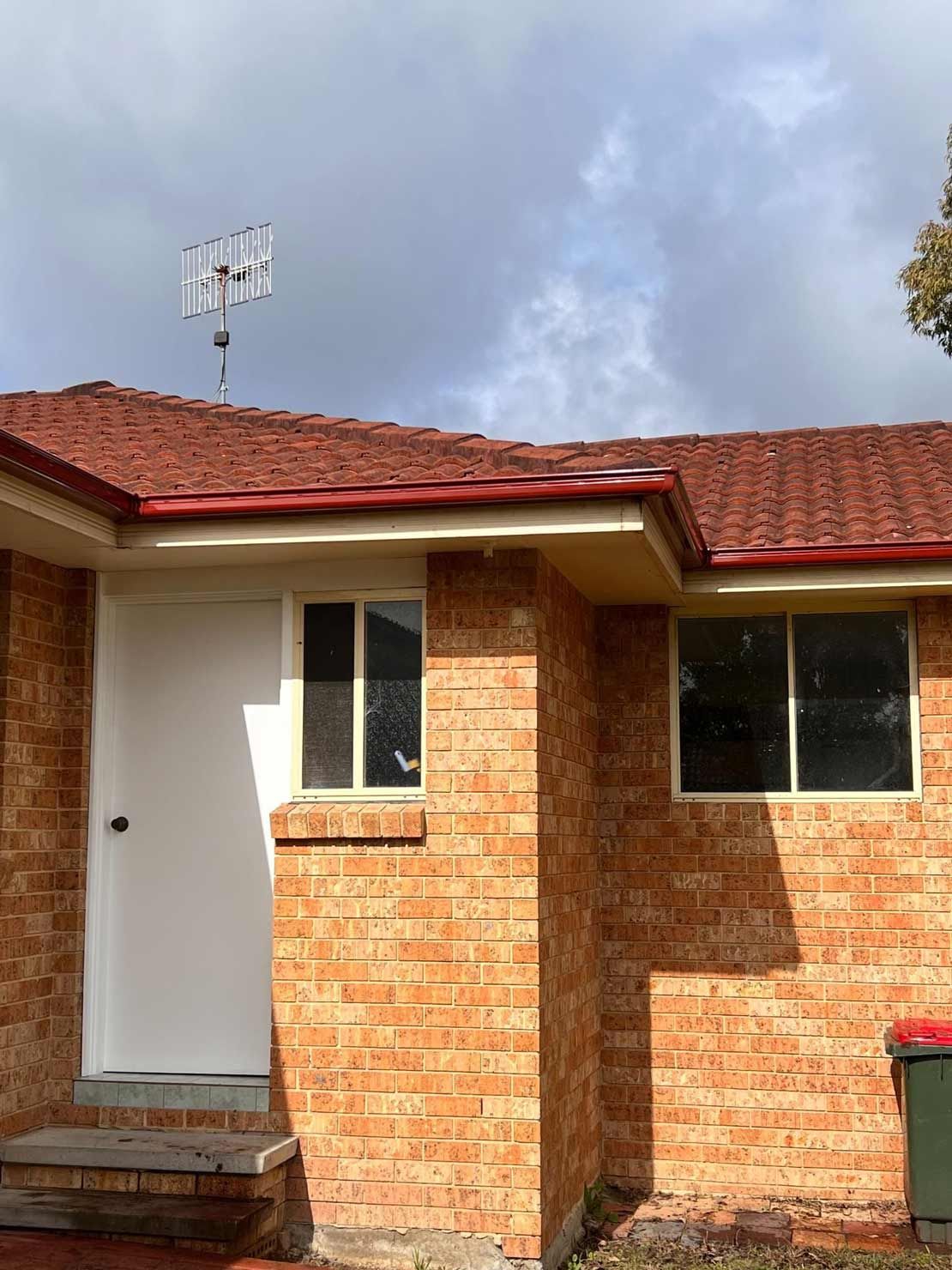 A Small Brick House With a Red Roof and a White Door — Gutterworx in Wamberal, NSW