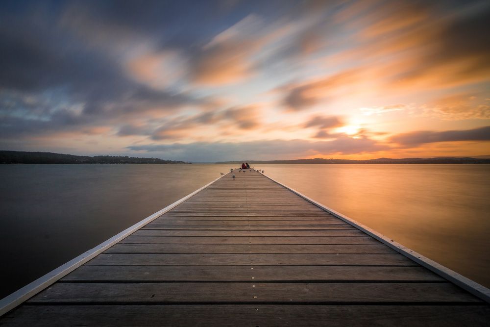 A Long Wooden Dock Leading Into a Body of Water at Sunset — Gutterworx in Long Jetty, NSW