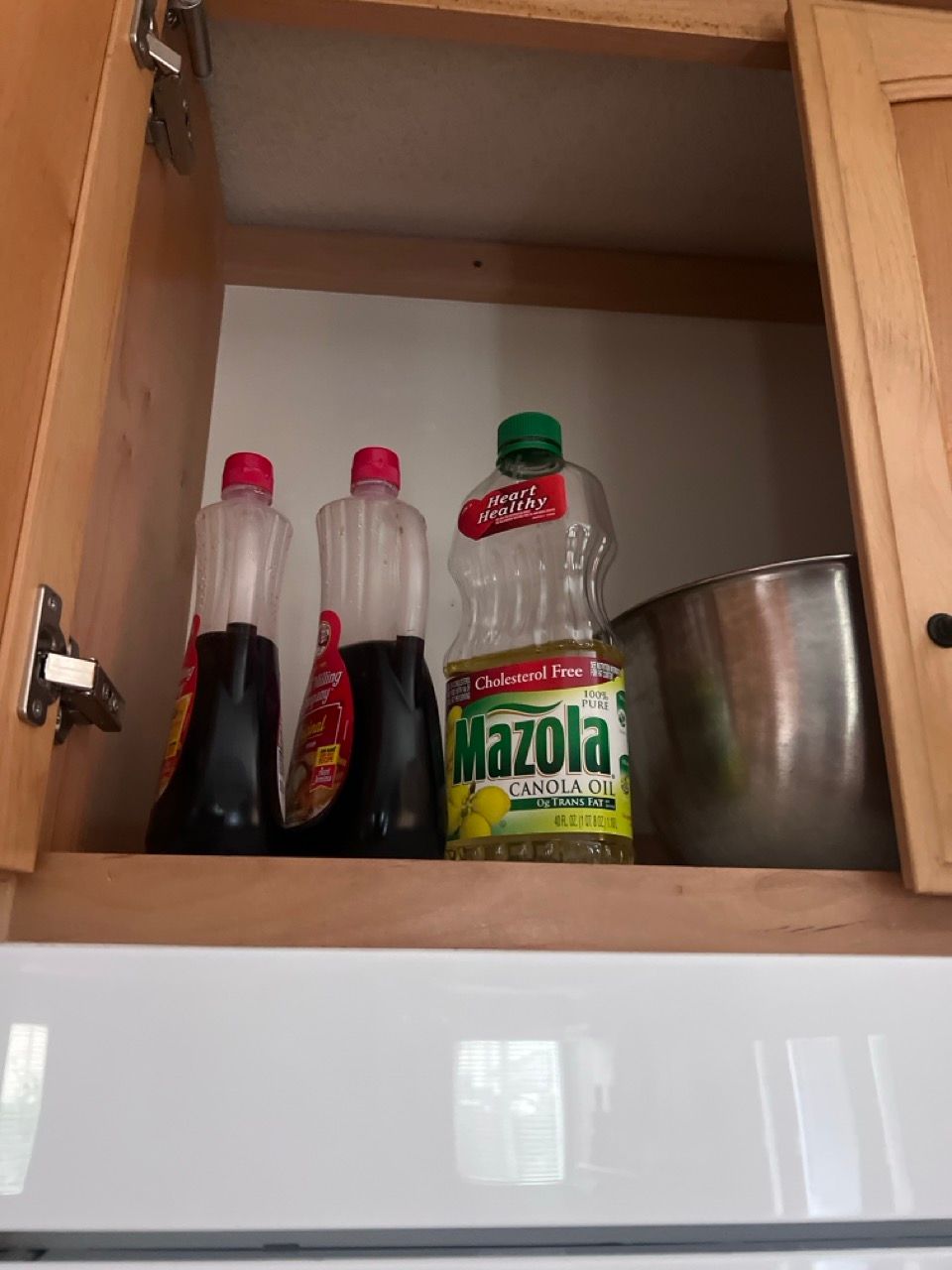 A bottle of mazola sits on a shelf in a cabinet