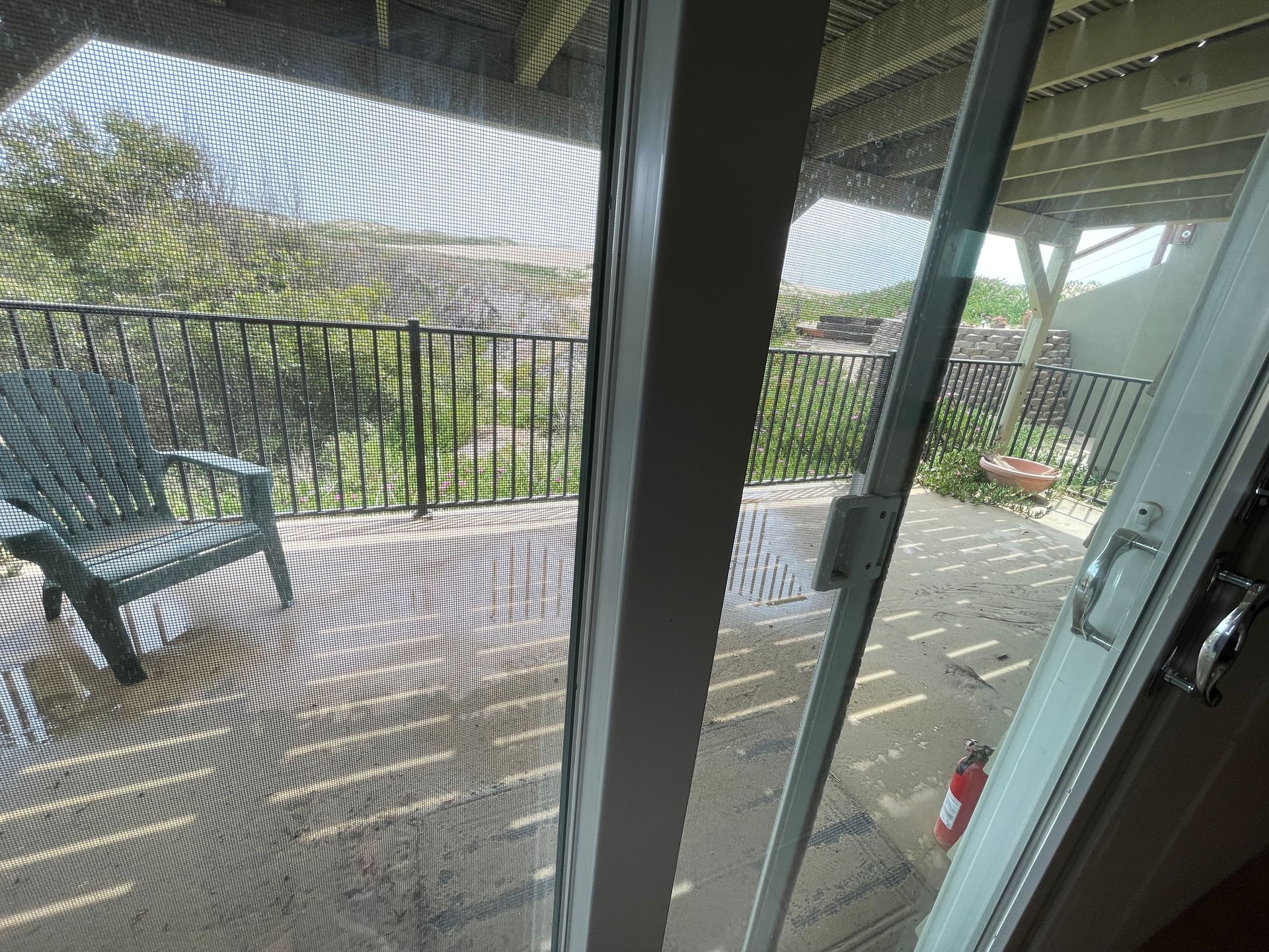 A sliding glass door leading to a deck with a chair and a fire extinguisher.