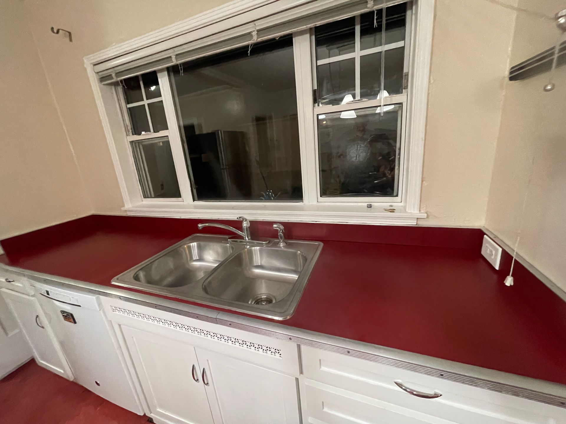 Kitchen with red countertop, double sink, and white cabinets beneath a window.
