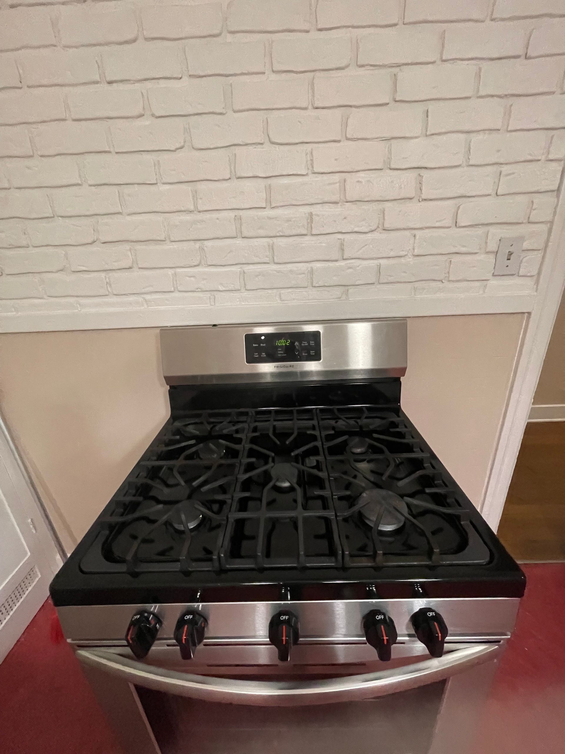 Stainless steel gas range stove with black grates and knobs in a kitchen.