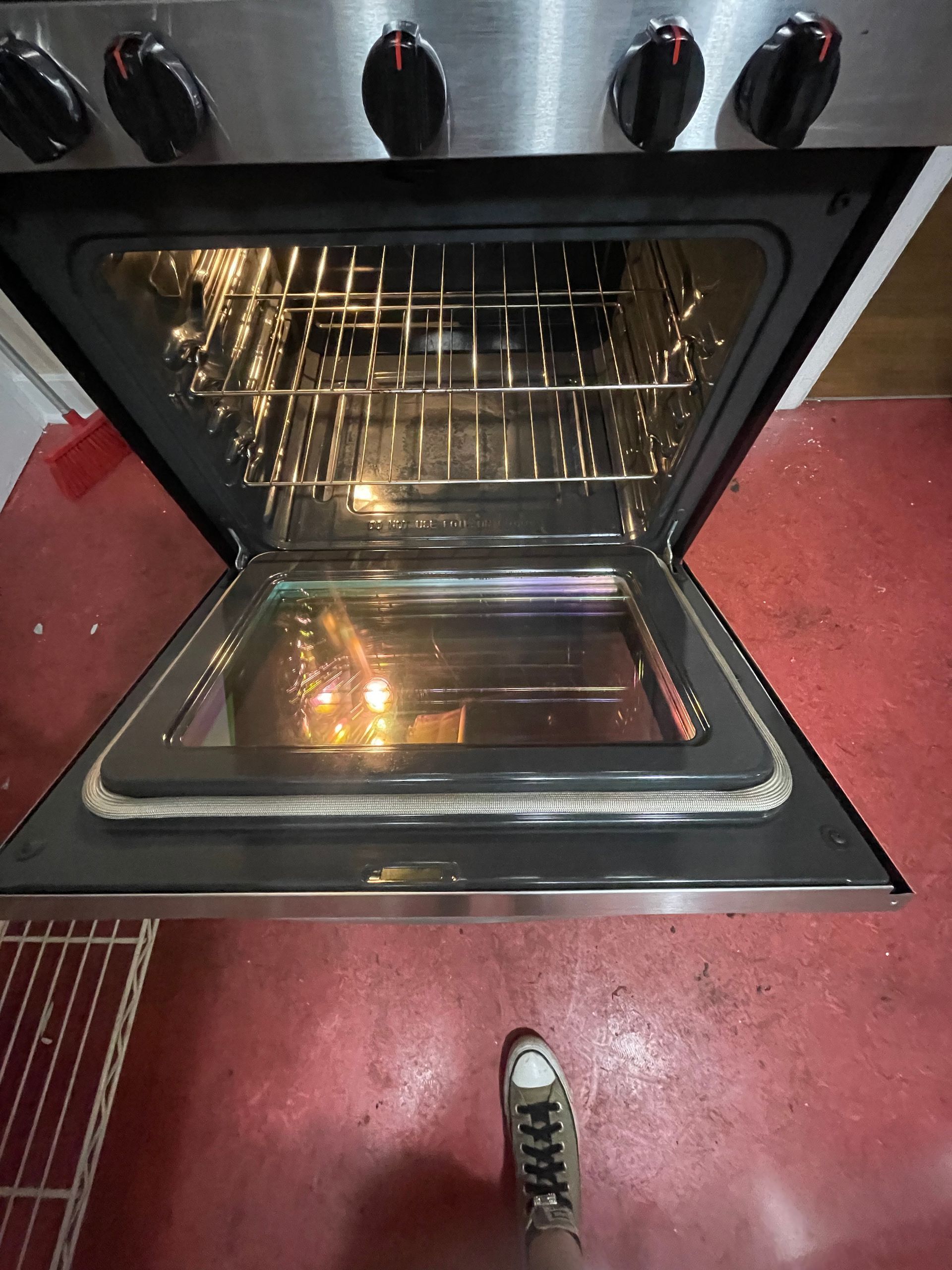 Open oven with light on, showing racks. Black knobs and stainless steel frame.
