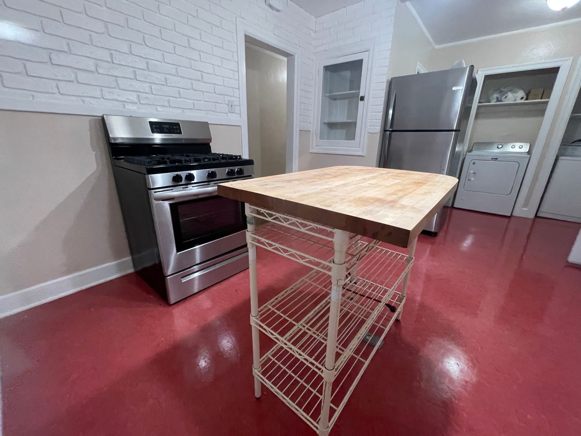 Kitchen with a stainless steel stove, butcher block island, refrigerator, and washer. Red floor.