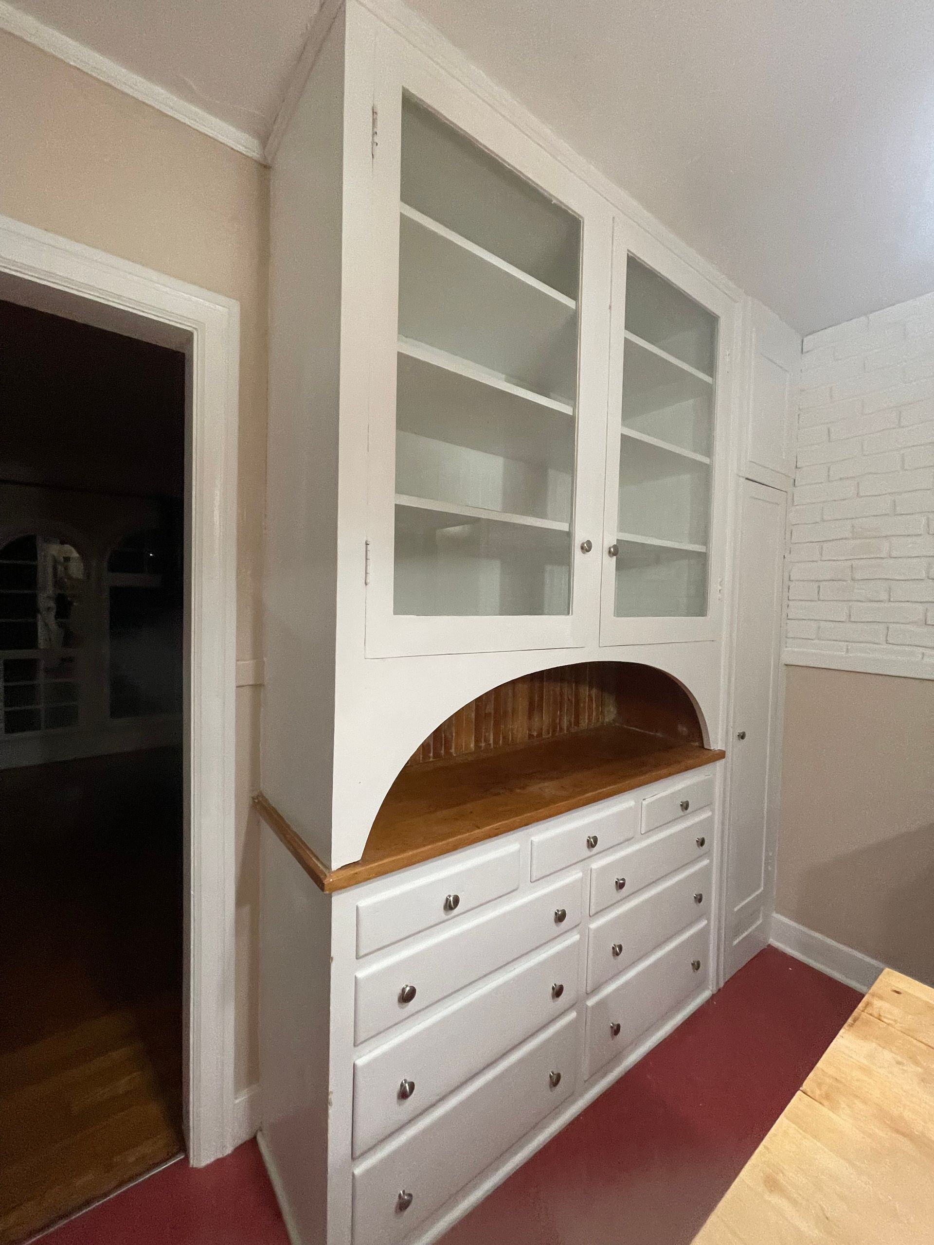White built-in cabinet with glass doors and drawers. Wooden countertop and arch detail.  Interior setting.