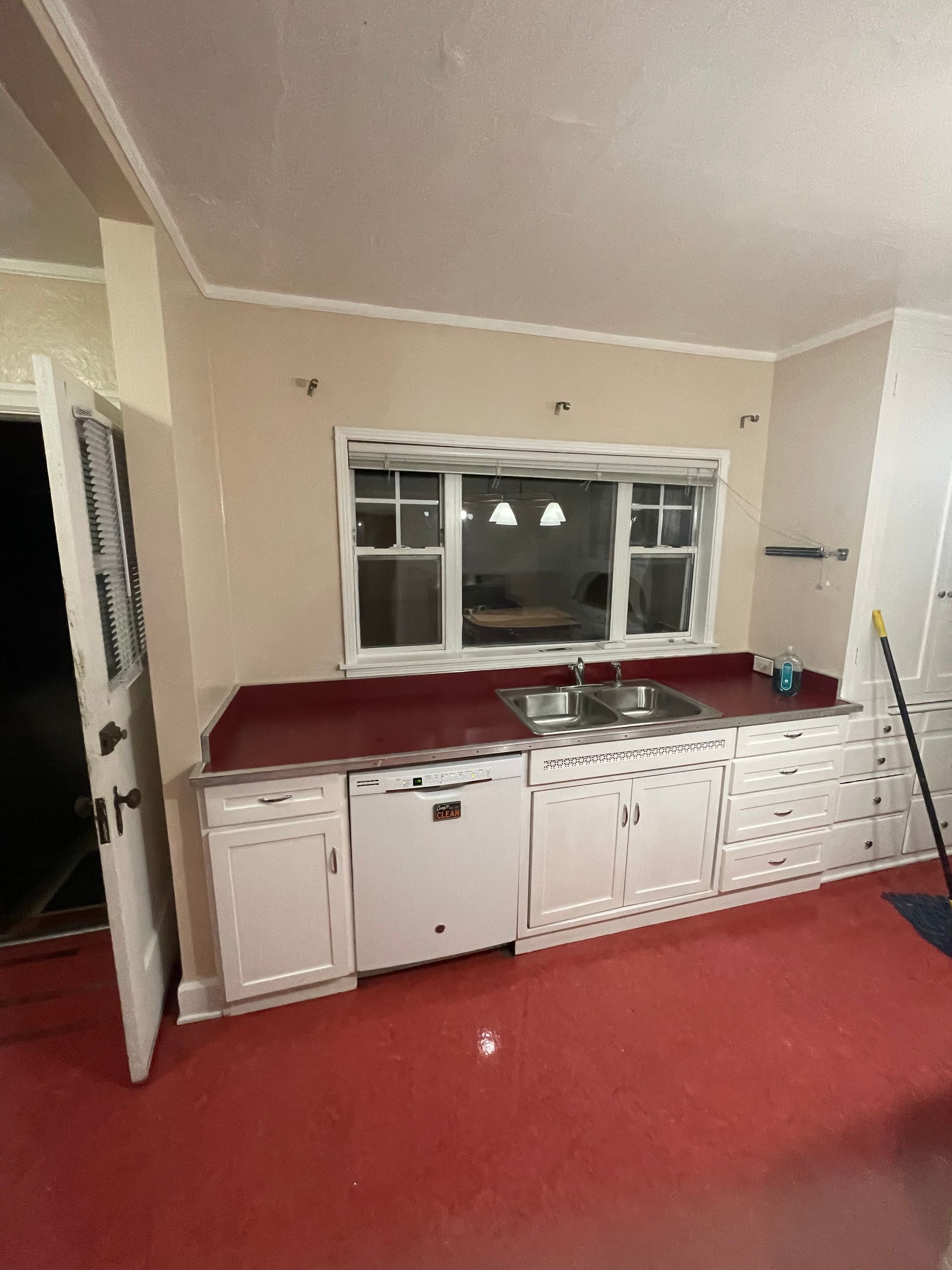 Kitchen with red countertops and floor, white cabinets, window, and a partially open door.