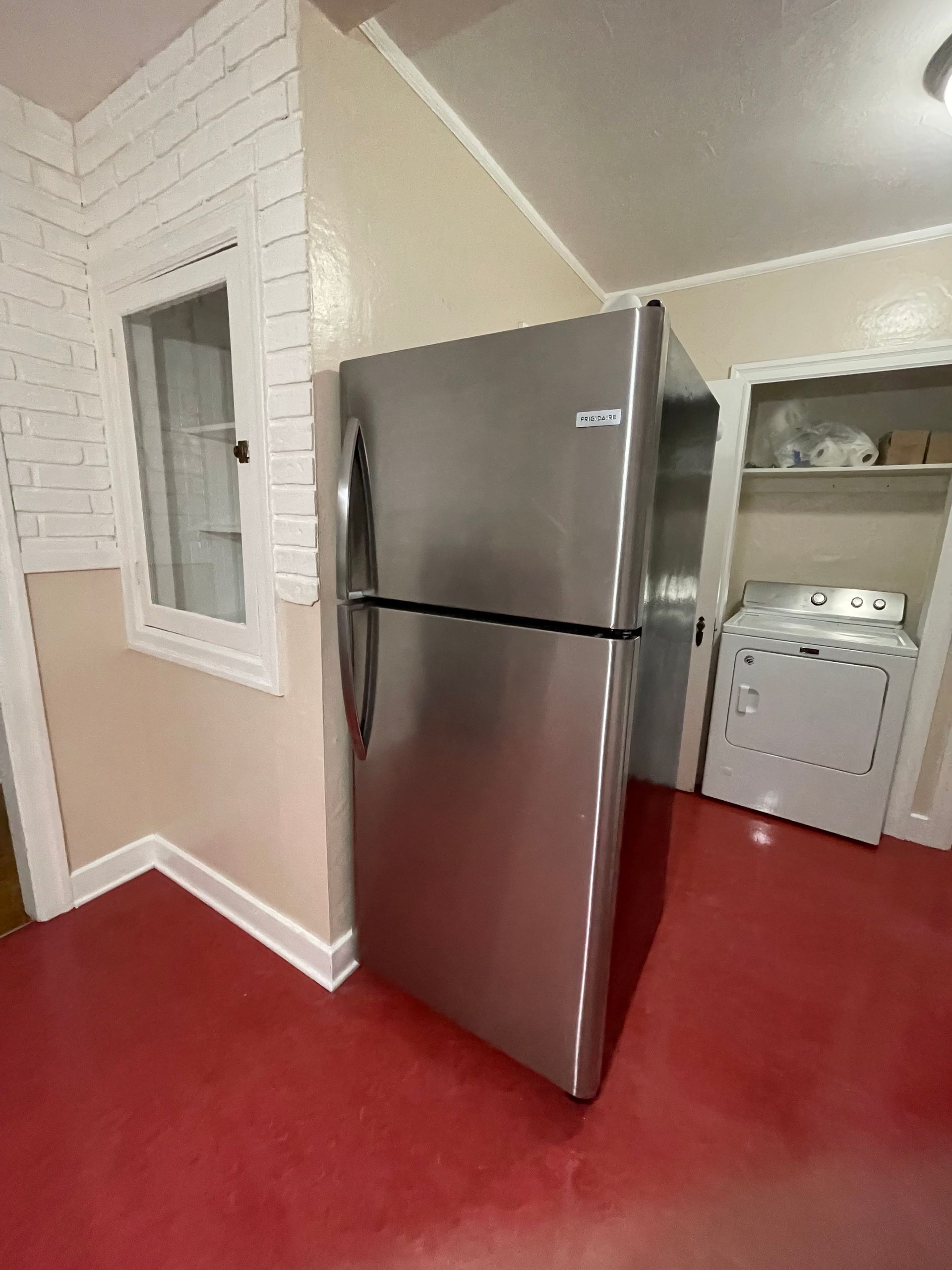 Stainless steel refrigerator in a kitchen with red flooring, and a washer/dryer in the background.