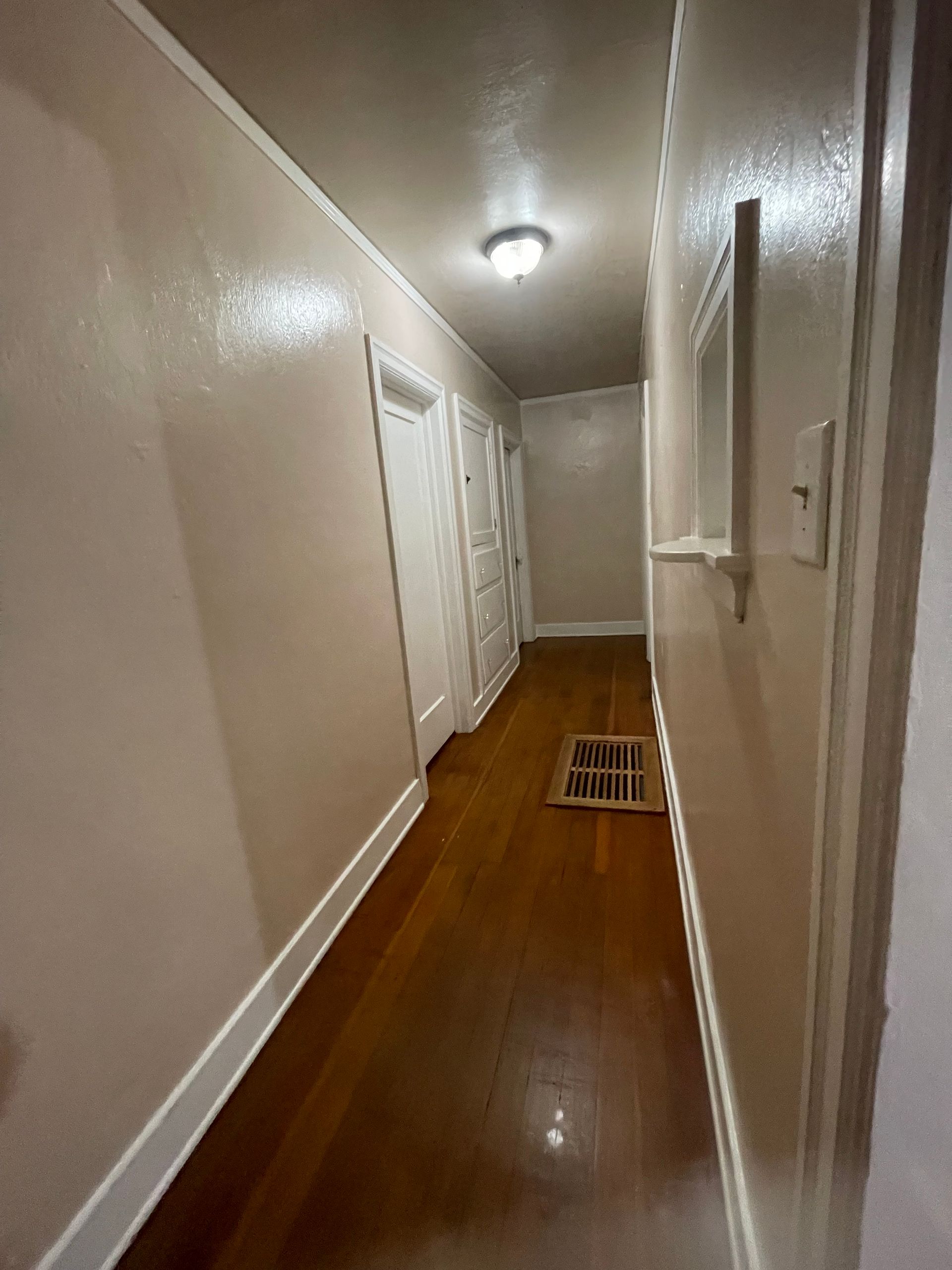 Narrow hallway with glossy wood floors, pale walls, and several closed doors.