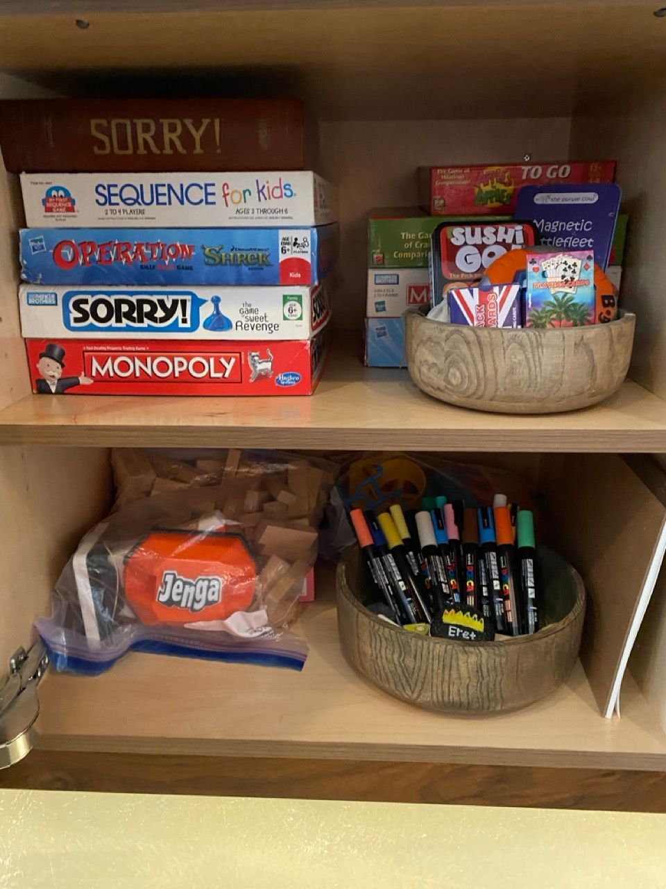 A shelf with a stack of board games including monopoly and sorry