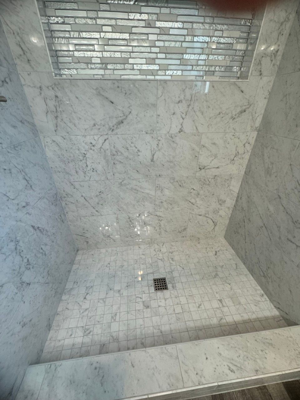A shower stall with marble tiles and a drain in a bathroom.