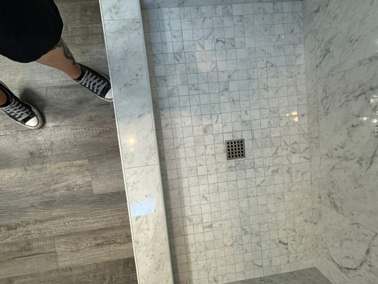 A person is standing in a shower with a drain on the floor.