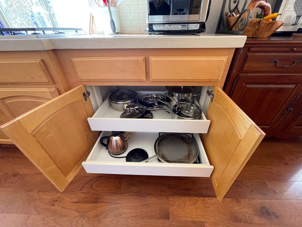 A kitchen cabinet with two drawers filled with pots and pans.