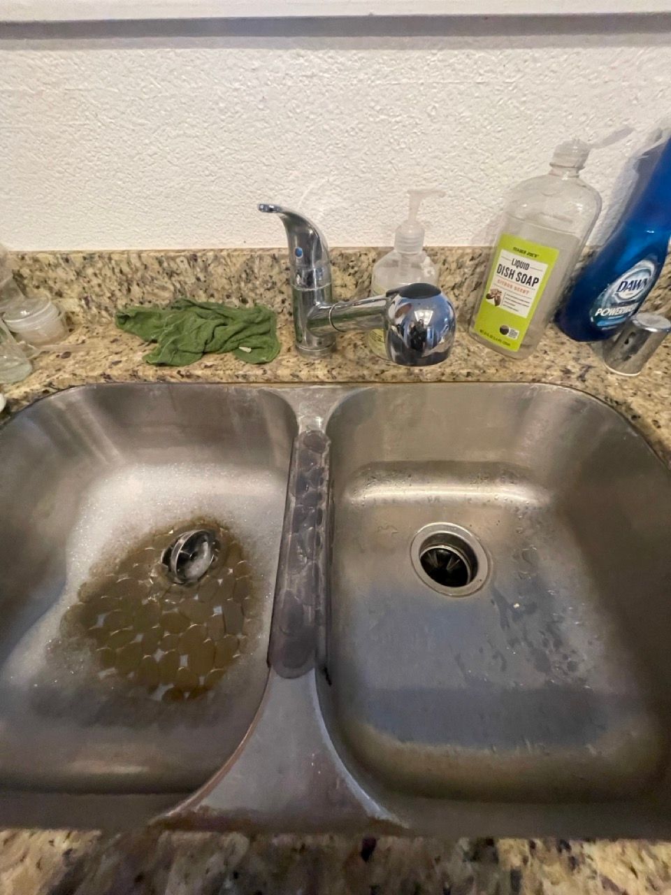 A stainless steel kitchen sink with a soap dispenser on the counter.