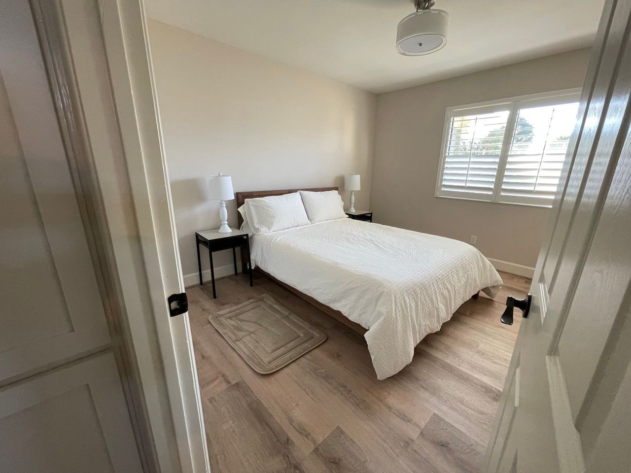 A bedroom with a bed , nightstand , lamps and a window.