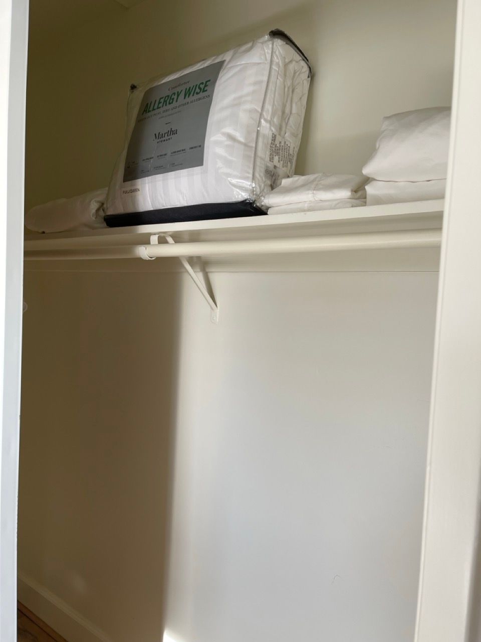 A closet with a pillow and sheets on the shelf